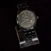 A sleek black Rado wristwatch with a metal strap displayed on a transparent stand against a dark background.