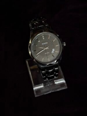 A sleek black Rado wristwatch with a metal strap displayed on a transparent stand against a dark background.