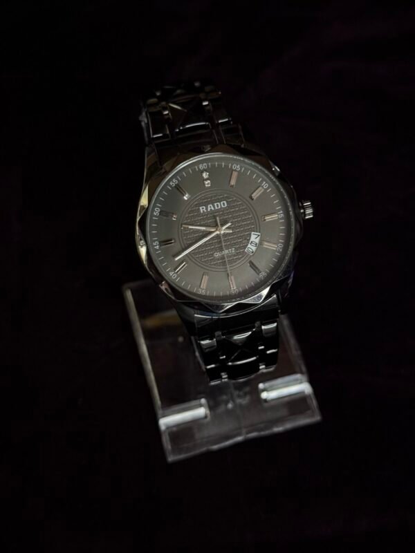 A sleek black Rado wristwatch with a metal strap displayed on a transparent stand against a dark background.